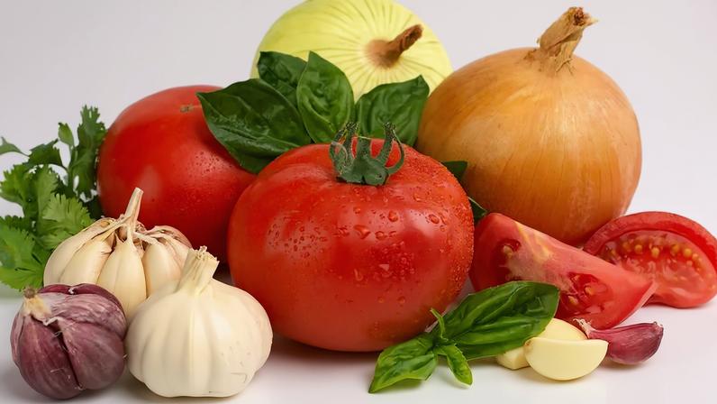 Tomates vermelhos frescos com gotas de água, cebolas amarela e branca, alhos e folhas de manjericão e coentro sobre fundo branco