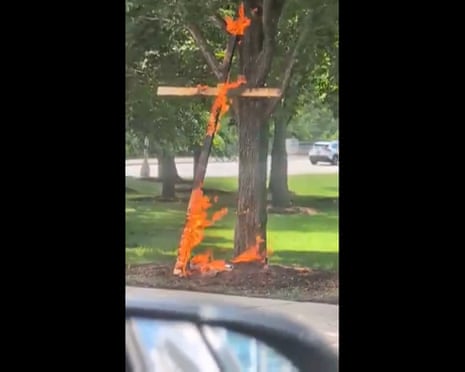This screenshot from a video taken by motorist Keinika Carlton shows a wooden cross engulfed in flames as it leans against a tree in Grant Park, Chicago, 9 July 2026.