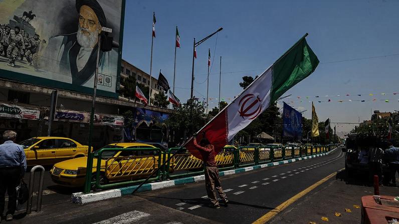 A worker raises a pole bearing the Iranian flag at Enghelab Square in Tehran