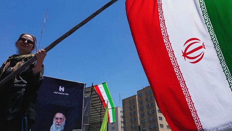 A woman waves an Iranian flag in front of a poster of the Supreme Leader Ayotollah Ali Khemenei in Tehran