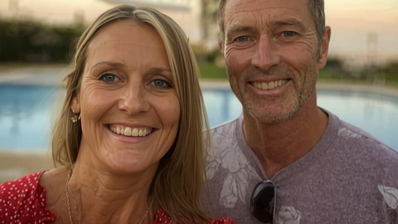 Craig and Lindsay Foreman pose together by a swimming pool with palm trees in the background