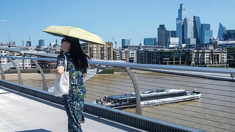A pedestrian shelters from the sun with an umbrella on the Millennium Bridge in London. A red weather warning means ‘dangerous weather is expected’. Photograph: Amer Ghazzal/Shutterstock