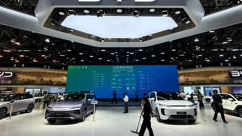 A large exhibition booth displays electric vehicles under a BYD logo, with visitors walking through the space