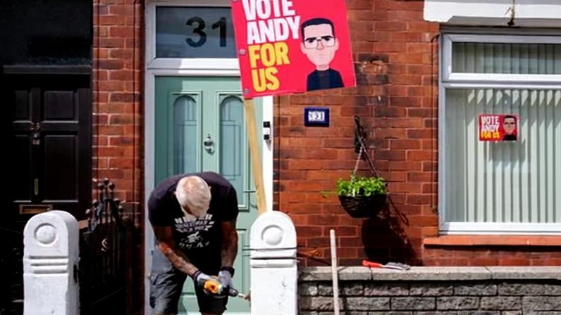 A man repairs a gate next to a Labour by-election campaign placard depicting Andy Burnham.
