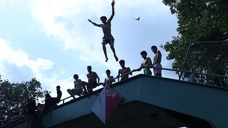 A person jumps off a bridge into the Canal Saint-Martin as public swimming having been allowed earlier on part of it due to rising of temperatures