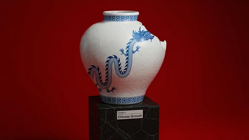 A studio shot of an artifact displayed on a black, textured stone pedestal against a solid red background. The artifact is a white porcelain vase with a cracked glaze texture and a large, serpentine blue dragon painted on its side. Geometric blue patterns decorate the rim and base of the vase. A large chunk is missing from the upper right side of the vessel, showing a broken edge. The front of the pedestal features a small white label that reads "EXHIBIT 4: Chinese Growth".
