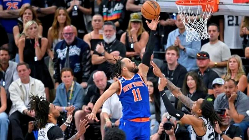 Armador do New York Knicks, Jalen Brunson (11), avança enquanto o armador do San Antonio Spurs, Devin Vassell (24), e o armador Dylan Harper (2) defendem durante o segundo tempo do Jogo 5 das Finais da NBA, neste sábado