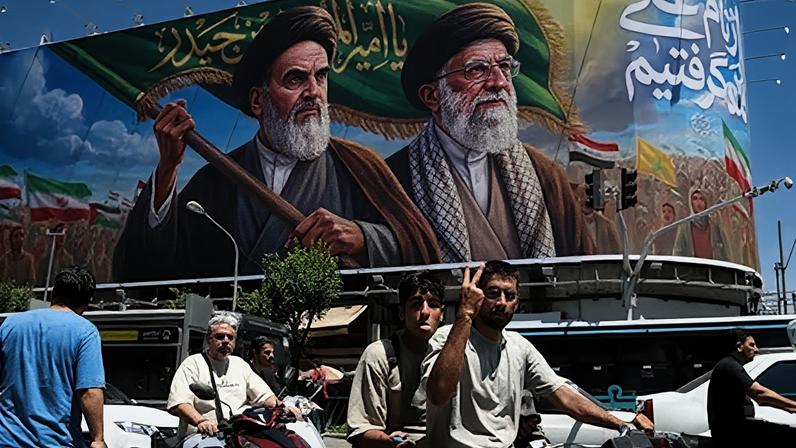 Un iraní hace el gesto de la victoria al pasar en coche junto a una valla publicitaria en la que aparecen los difuntos líderes supremos iraníes, Ruhollah Jomeini y Ali Jameneí, en una calle de Teherán, Irán, el 15 de junio de 2026.
