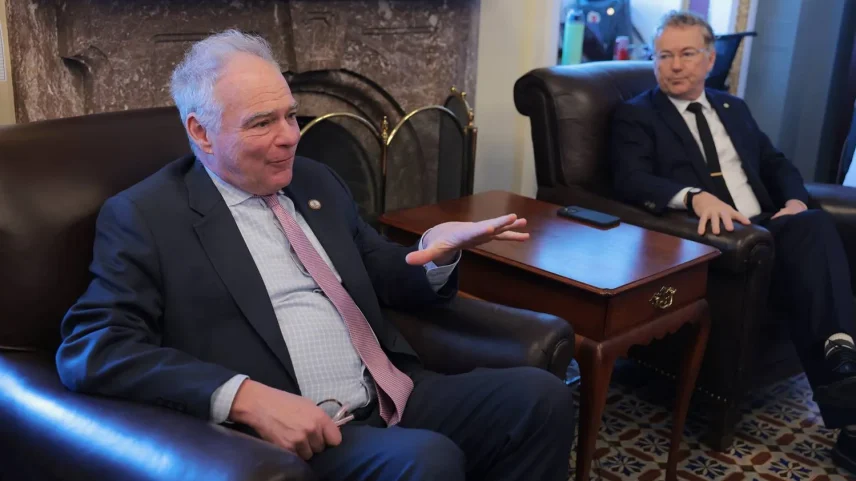 Sen. Tim Kaine and Sen. Rand Paul are seen sitting in chairs, with a table between them, talking to reporters.