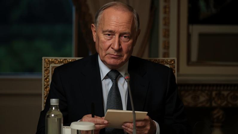 Russian President Vladimir Putin speaks into a microphone while holding papers.