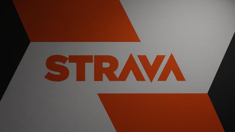 The Strava logo against a black, orange, and gray background.