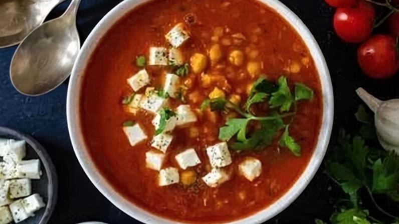 Sopa de lentilha e grão-de-bico com cubos de queijo feta, servida em tigela branca e decorada com folhas de salsa
