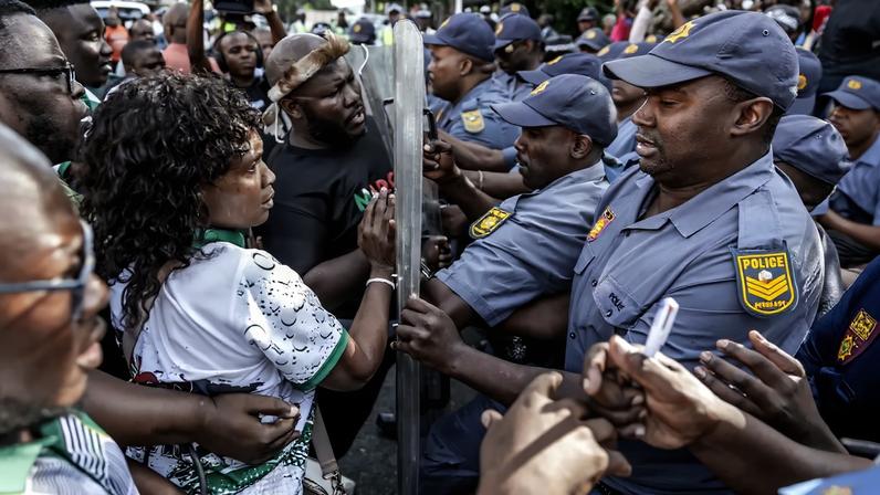 Demonstrators are shown from the side as the police (right) try to hold them back.
