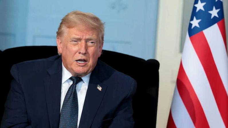 U.S. President Donald Trump is seen talking while sitting near a United States flag.
