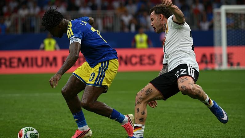 O meio-campista de Curaçao, Leandro Bacuna, disputa a bola com o zagueiro alemão David Raum, durante a partida de futebol do Grupo E da Copa do Mundo de 2026. Créditos: Foto por RONALDO SCHEMIDT / AFP