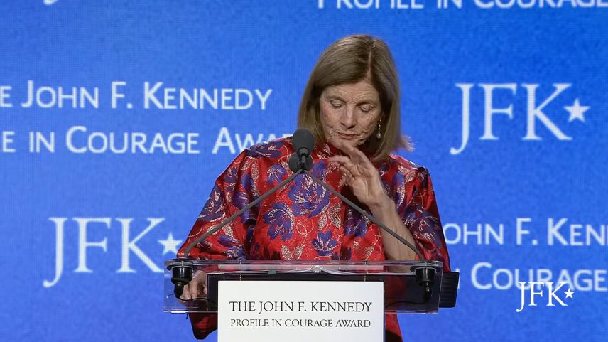 Caroline Kennedy looking tearful at a podium with a blue background featuring the JFK Profile in Courage Award logo.