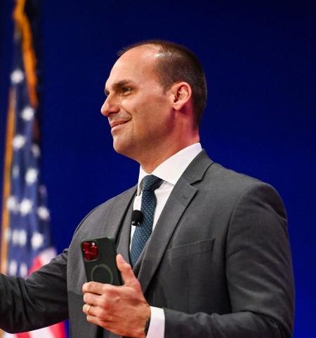 Com o celular na mão, o ex-deputado federal Eduardo Bolsonaro acena do palco da conferência conservadora CPAC em Dallas, Texas