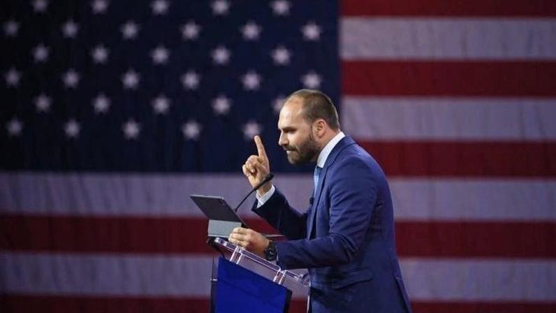 Deputado federal Eduardo Bolsonaro discursa em frente à bandeira dos Estados Unidos