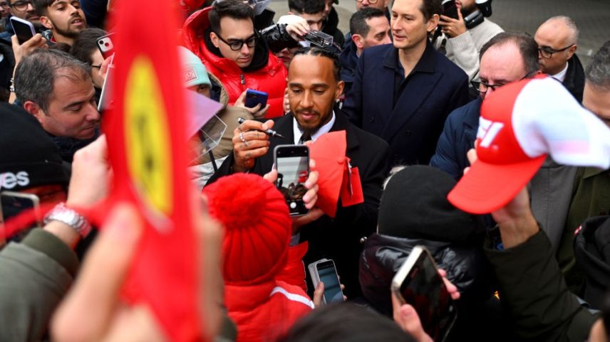 Lewis Hamilton e John Elkann, ao fundo, falam com jornalistas em Maranello, em janeiro de 2025 — Foto: Rudy Carezzevoli/Getty Images
