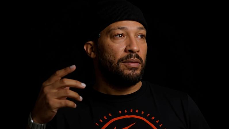 Jalen Brunson in a black beanie and Knicks t-shirt, gesturing with his hand.