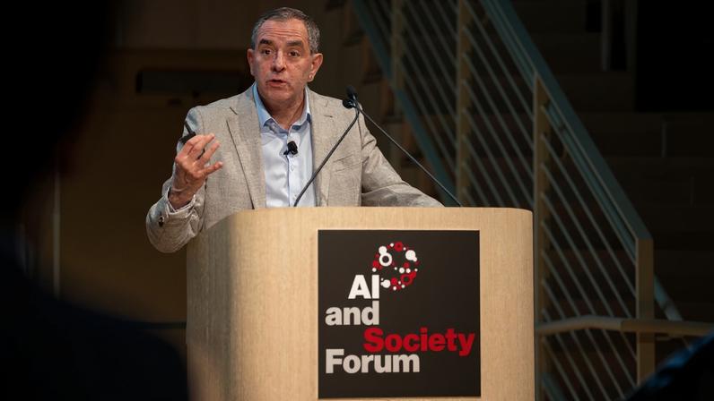 David Autor speaks from an indoor lectern that has a sign reading "AI and Society Forum."