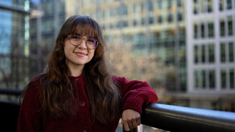 Giselle Valdes poses leaning on a railing, with large office buildings in the background