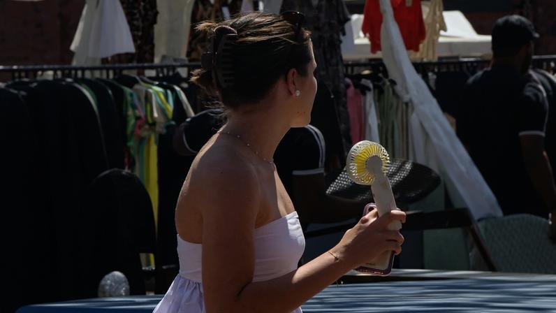 A woman cools herself with a handheld electric fan