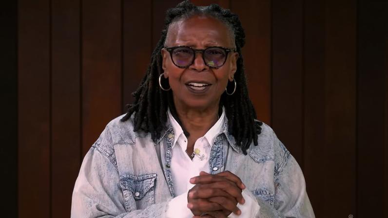 Whoopi Goldberg on "The View" holding her cue cards with "Hot Topics" visible on screen.