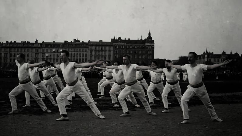 Grupo de homens em uniformes brancos de ginástica, com bigodes, realizando exercícios sincronizados ao ar livre, com braços estendidos e pernas afastadas, em frente a um grande edifício urbano e uma multidão ao fundo