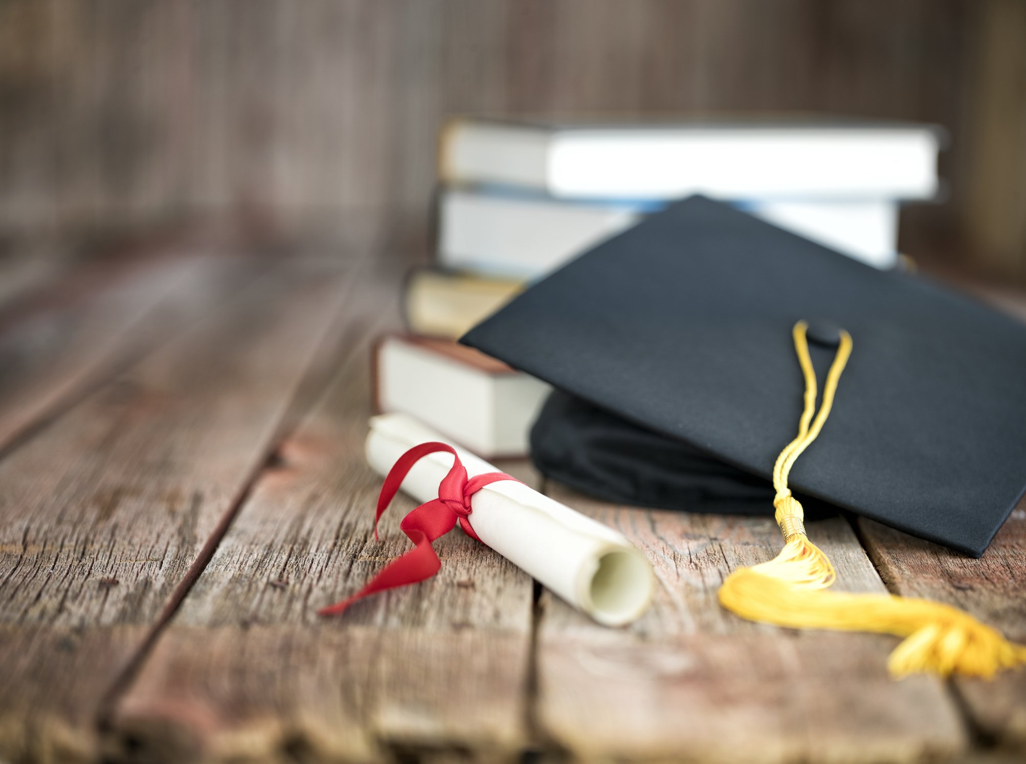Capelo de formatura e diploma com uma pilha de livros sobre um fundo de madeira (Foto: Liliboas/Getty Images)