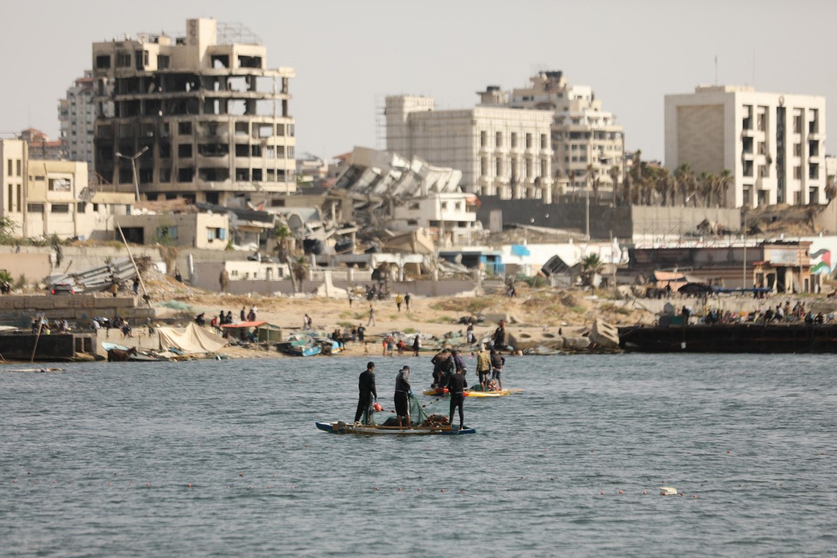 Israel intensifica restrições de banho e pesca no mar de Gaza em meio ao calor extremo Pescadores palestinos tentam pescar com barcos a remo e varas de pescar na costa da Cidade de Gaza, enquanto prédios danificados e destruídos são vistos ao fundo (Foto: DAWOUD ABO ALKAS / AFP).
